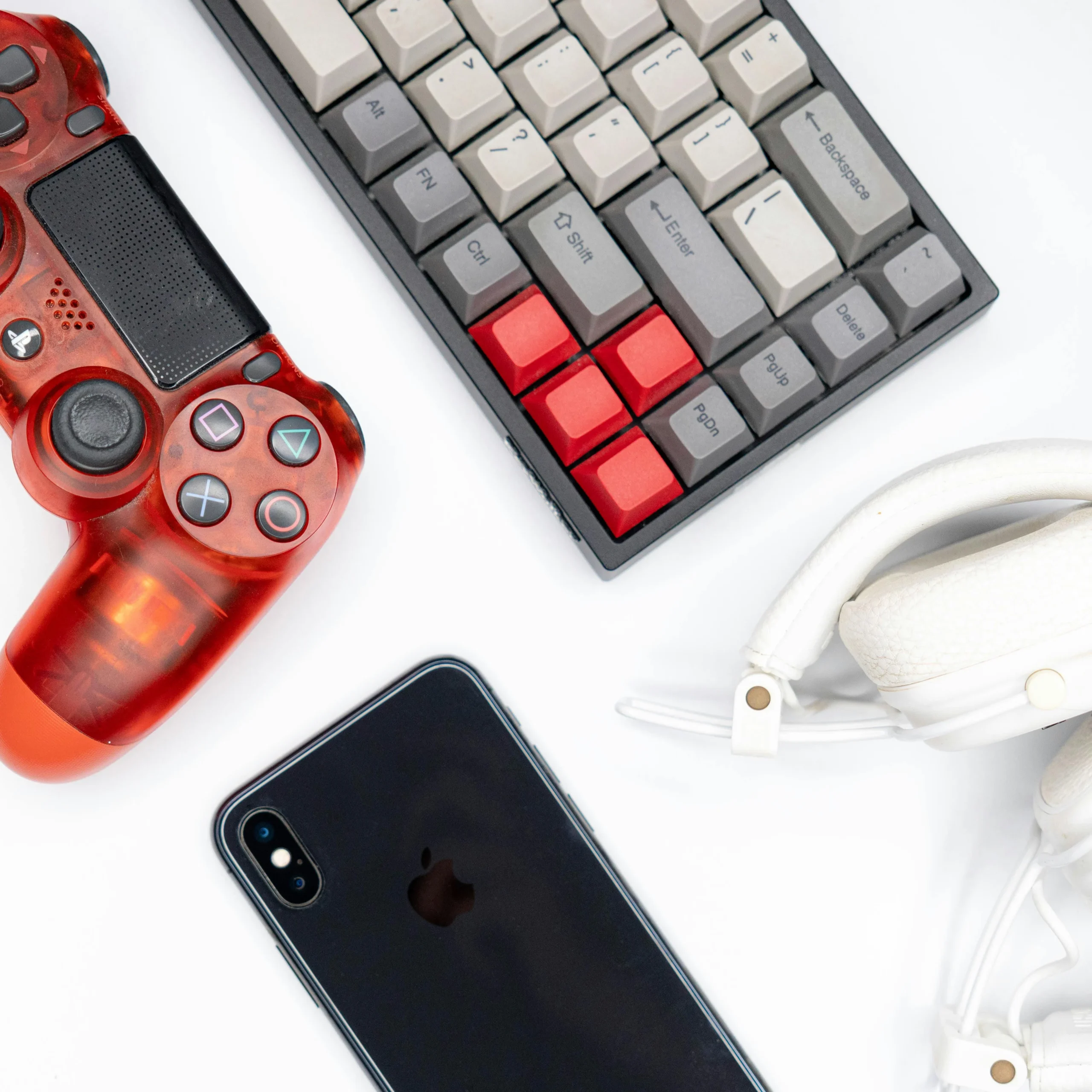 Red gaming controller, mechanical keyboard, smartphone, and headphones on white background – tech toys and gaming gear